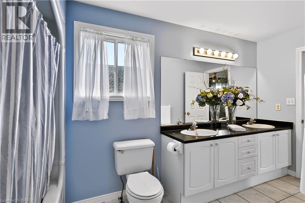 Double vanity with white cabinetry, dual sinks, black countertop, and an expansive wall mirror - 19 Hyslop Drive, Caledonia, ON