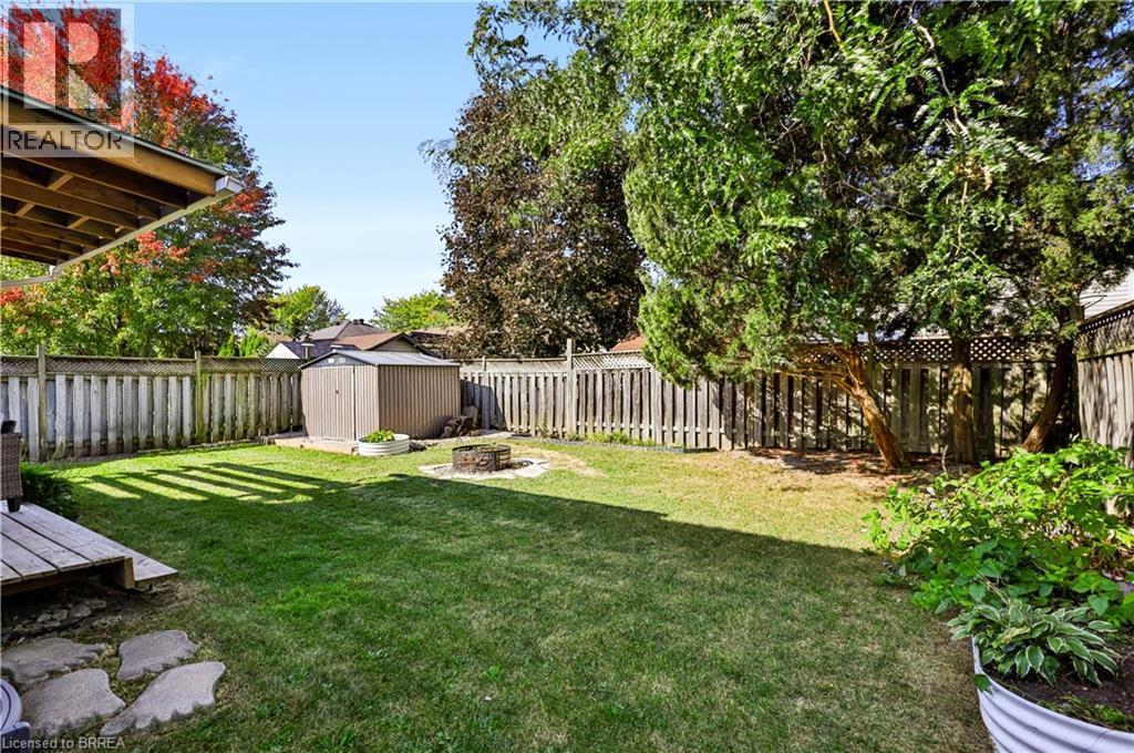 Expansive backyard featuring a manicured lawn, established trees, wood fencing, a storage shed, and a built-in fire pit - 19 Hyslop Drive, Caledonia, ON
