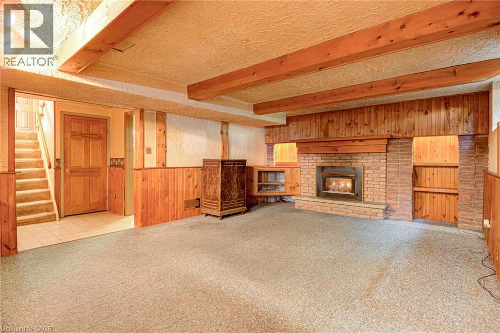 Brick fireplace with an integrated firebox and built-in shelving, wood paneling, exposed wood beams, and a carpeted floor - 8 Bonnylyn Drive, Kitchener, ON