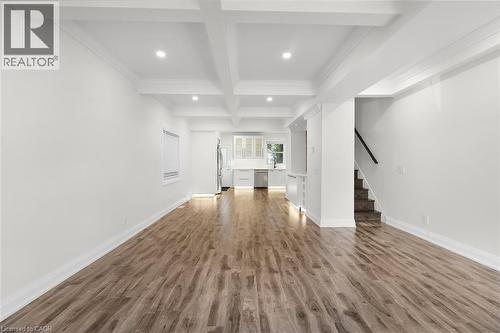 Spacious interior with wood-finish flooring, coffered ceiling, recessed lighting, and a modern kitchen featuring white cabinetry and stainless steel appliances - 73 Clinton Street, Hamilton, ON 