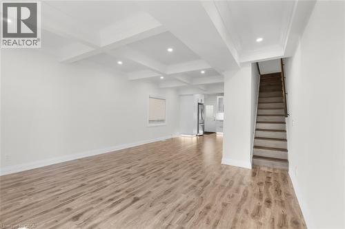 Spacious living area featuring wood-finish flooring, coffered ceiling with recessed lighting, and a window with blinds - 73 Clinton Street, Hamilton, ON 