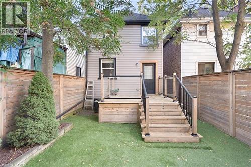 Hardscaped backyard featuring artificial turf, wood fencing, and a multi-level wood deck with black railings - 73 Clinton Street, Hamilton, ON 