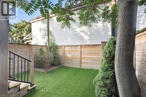 Enclosed outdoor space featuring horizontal wood fencing, artificial turf, wood steps with a black metal railing, and a raised planter bed - 73 Clinton Street, Hamilton, ON 