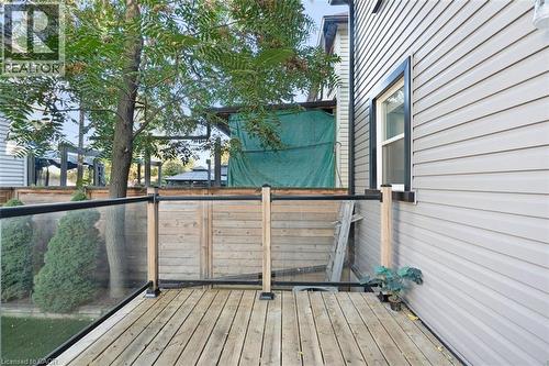 Wood-finish deck with glass panel railing and natural wood posts, complemented by light-toned siding and a black-framed window - 73 Clinton Street, Hamilton, ON 