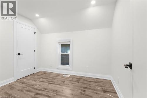 Recessed lighting illuminates this space featuring wood-finish flooring, a contemporary flat-panel door, and a window with blinds - 73 Clinton Street, Hamilton, ON 