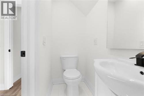 White ceramic tile flooring, pedestal sink with black faucet, contemporary mirror, and white toilet - 73 Clinton Street, Hamilton, ON 