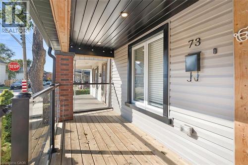 Front porch featuring wood-finish decking, brick column accents, and clear glass panel railings - 73 Clinton Street, Hamilton, ON 