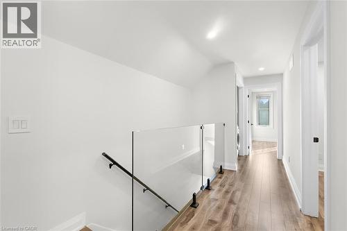 Hardwood-style flooring throughout, clear glass railing with a matte black handrail, and recessed lighting - 73 Clinton Street, Hamilton, ON 