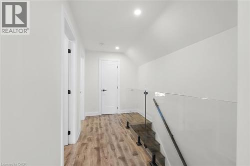 Wood-finish flooring, recessed lighting, white walls, white doors with dark hardware, and a glass panel stair railing - 73 Clinton Street, Hamilton, ON 