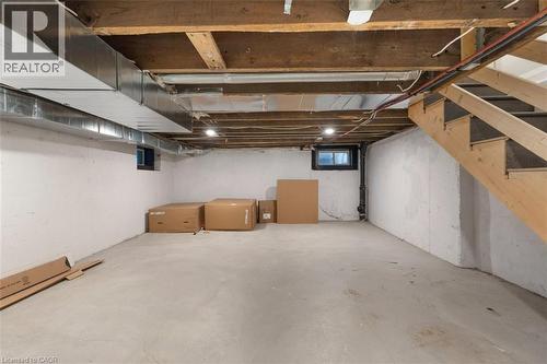 Unfinished basement with concrete floor, exposed wood ceiling joists, and a partial wooden staircase - 73 Clinton Street, Hamilton, ON 