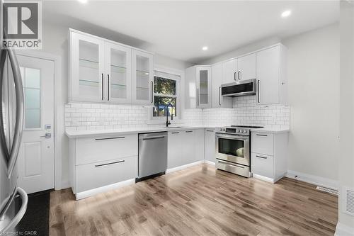 Modern kitchen featuring white cabinetry with black hardware, stainless steel appliances, a subway tile backsplash, and wood-finish flooring - 73 Clinton Street, Hamilton, ON 