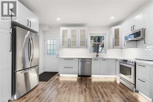 White cabinetry with black hardware, wood-finish flooring, subway tile backsplash, stainless steel appliances, and recessed lighting - 73 Clinton Street, Hamilton, ON 