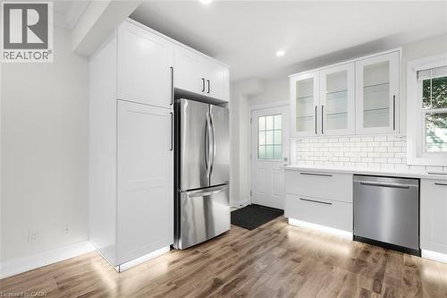 Modern kitchen featuring white cabinetry, stainless steel appliances, wood-finish flooring, subway tile backsplash, and recessed lighting - 73 Clinton Street, Hamilton, ON 