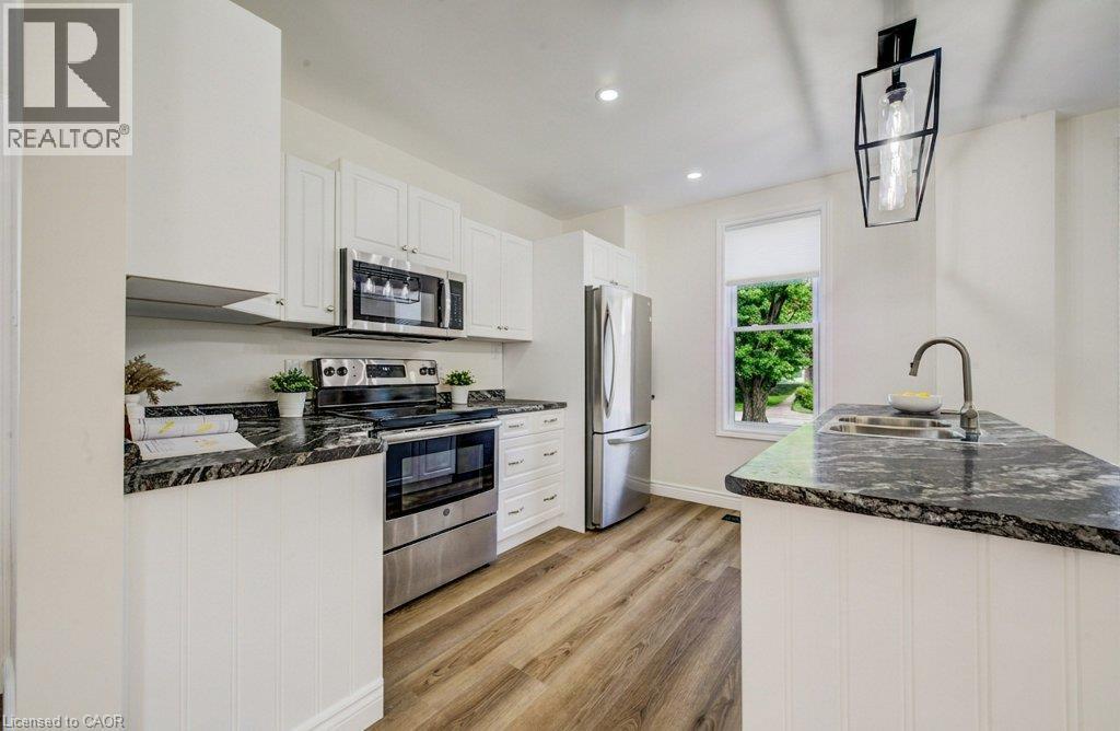 Kitchen featuring stainless steel appliances, dark granite countertops, white cabinetry, wood-finish flooring, and a pendant light fixture - 185 Strange Street, Kitchener, ON - Indoor Photo Showing Kitchen With Double Sink With Upgraded Kitchen