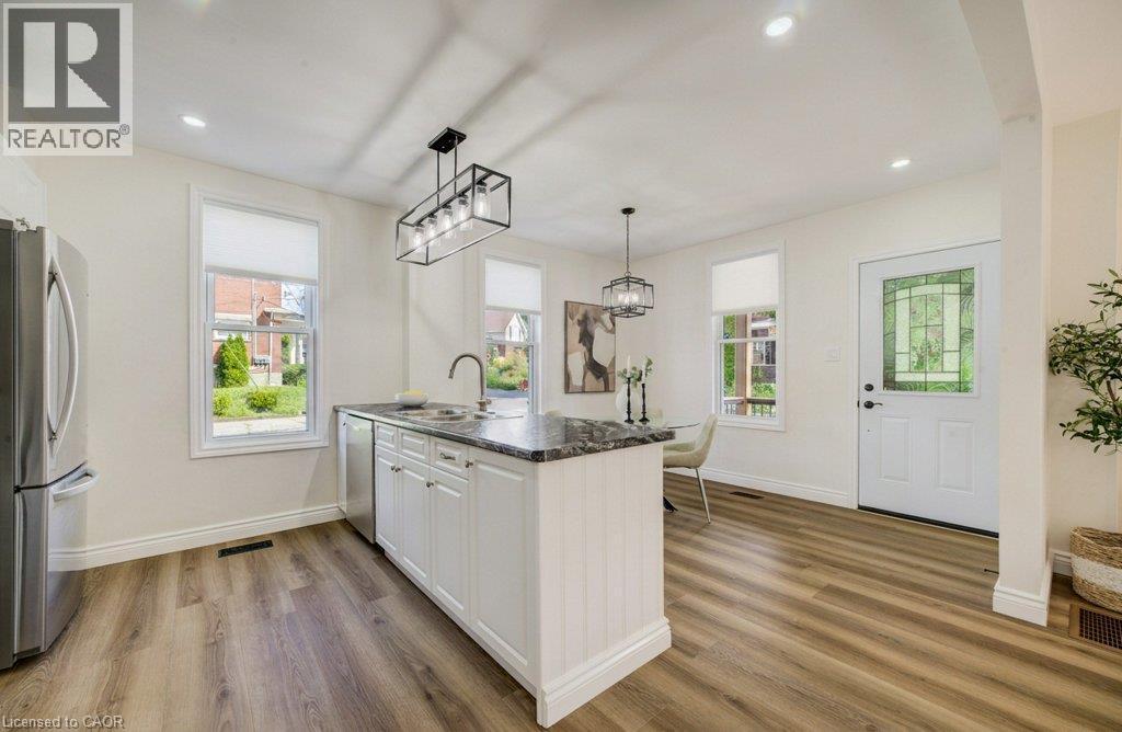 Open-concept kitchen with wood-finish flooring, white cabinetry, dark stone countertops, and stainless steel appliances - 185 Strange Street, Kitchener, ON - Indoor Photo Showing Kitchen