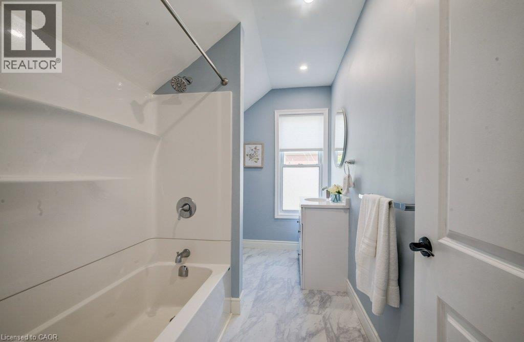 Tub/shower combination with a curved shower rod, vanity with an integrated sink, window with privacy blind, and recessed lighting - 185 Strange Street, Kitchener, ON - Indoor Photo Showing Bathroom