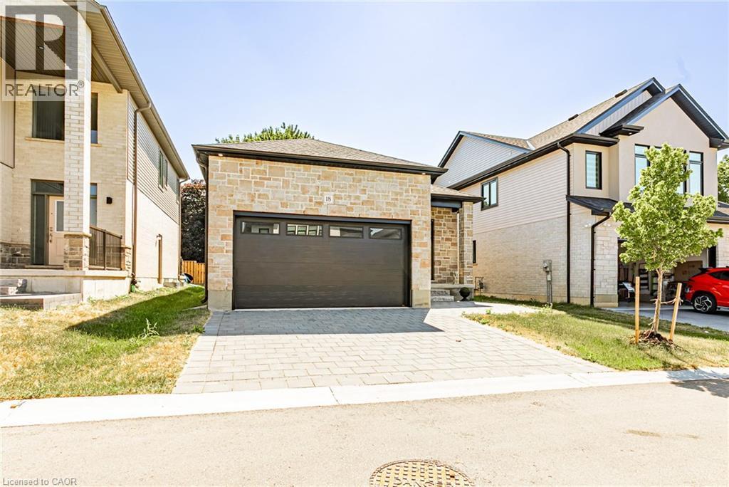 Stone exterior with a dark garage door, paver driveway, and a newly planted tree - 7966 Fallon Drive Unit# 18, Lucan Biddulph (Twp), ON - Outdoor