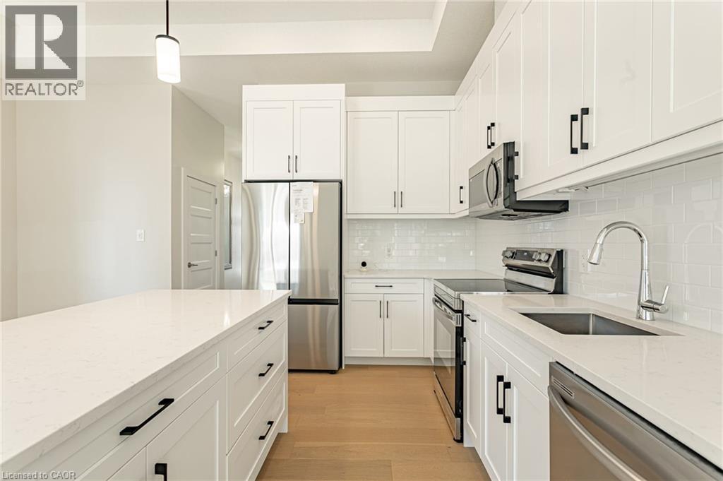 Kitchen featuring an island with white cabinetry and dark hardware, stainless steel appliances, light wood-finish flooring, white subway tile backsplash, and white countertops - 7966 Fallon Drive Unit# 18, Lucan Biddulph (Twp), ON - Indoor Photo Showing Kitchen With Upgraded Kitchen