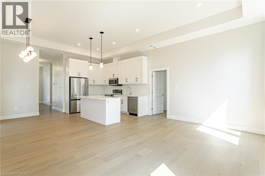 Open-concept living space with light wood-finish flooring, white kitchen cabinetry, stainless steel appliances, and a central kitchen island - 7966 Fallon Drive Unit# 18, Lucan Biddulph (Twp), ON - Indoor Photo Showing Kitchen