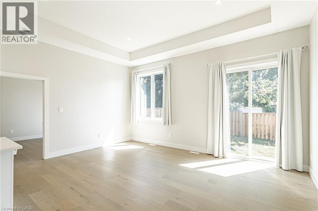 Recessed ceiling lighting, tray ceiling detail, wood-finish flooring, sliding glass door, and white trim - 7966 Fallon Drive Unit# 18, Lucan Biddulph (Twp), ON - Indoor Photo Showing Other Room