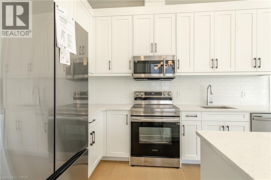 White shaker cabinetry, stainless steel appliances, subway tile backsplash, light-toned countertops, and wood-finish flooring - 7966 Fallon Drive Unit# 18, Lucan Biddulph (Twp), ON - Indoor Photo Showing Kitchen With Upgraded Kitchen