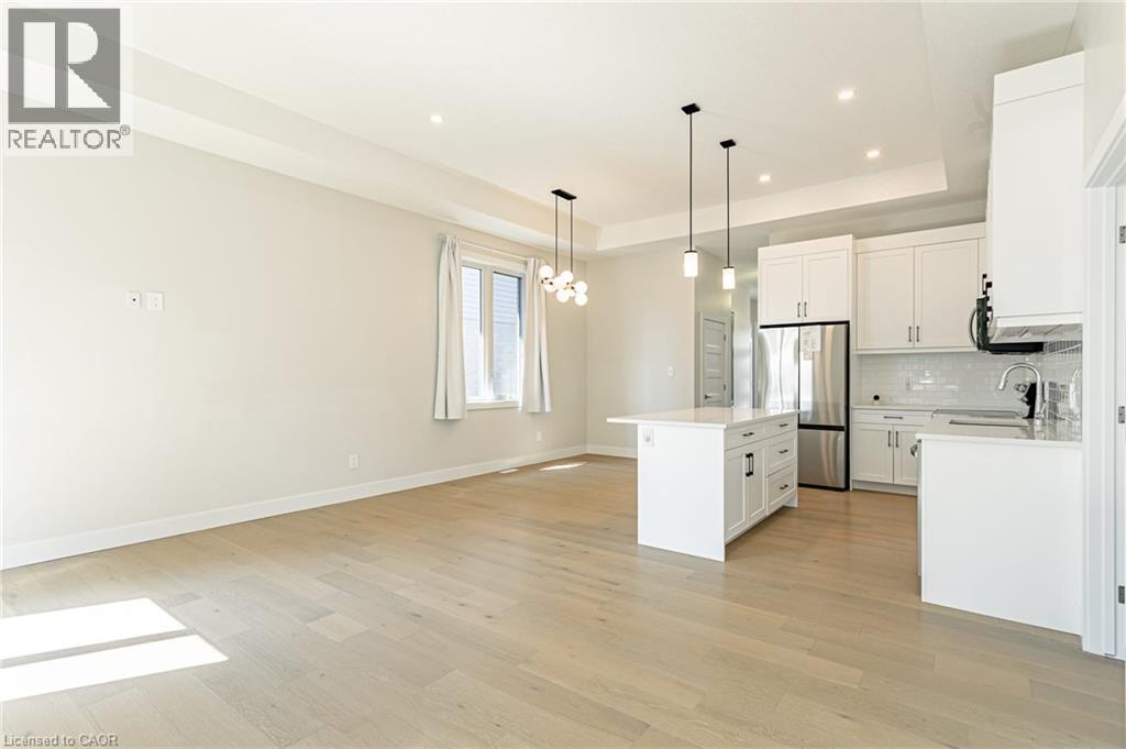 Open-concept kitchen and living area featuring white cabinetry, stainless steel appliances, a central island with pendant lighting, wood-finish flooring throughout, and recessed ceiling lights with a - 7966 Fallon Drive Unit# 18, Lucan Biddulph (Twp), ON - Indoor Photo Showing Kitchen With Upgraded Kitchen