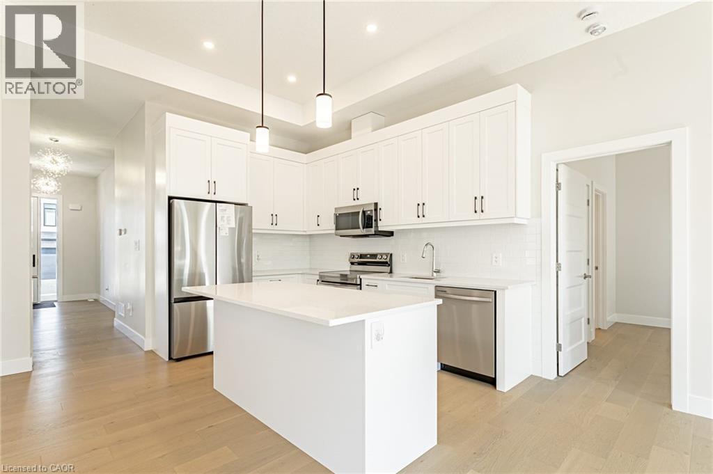 Kitchen featuring white cabinetry, stainless steel appliances, a center island with a solid surface countertop, white subway tile backsplash, and wood-finish flooring - 7966 Fallon Drive Unit# 18, Lucan Biddulph (Twp), ON - Indoor Photo Showing Kitchen With Upgraded Kitchen