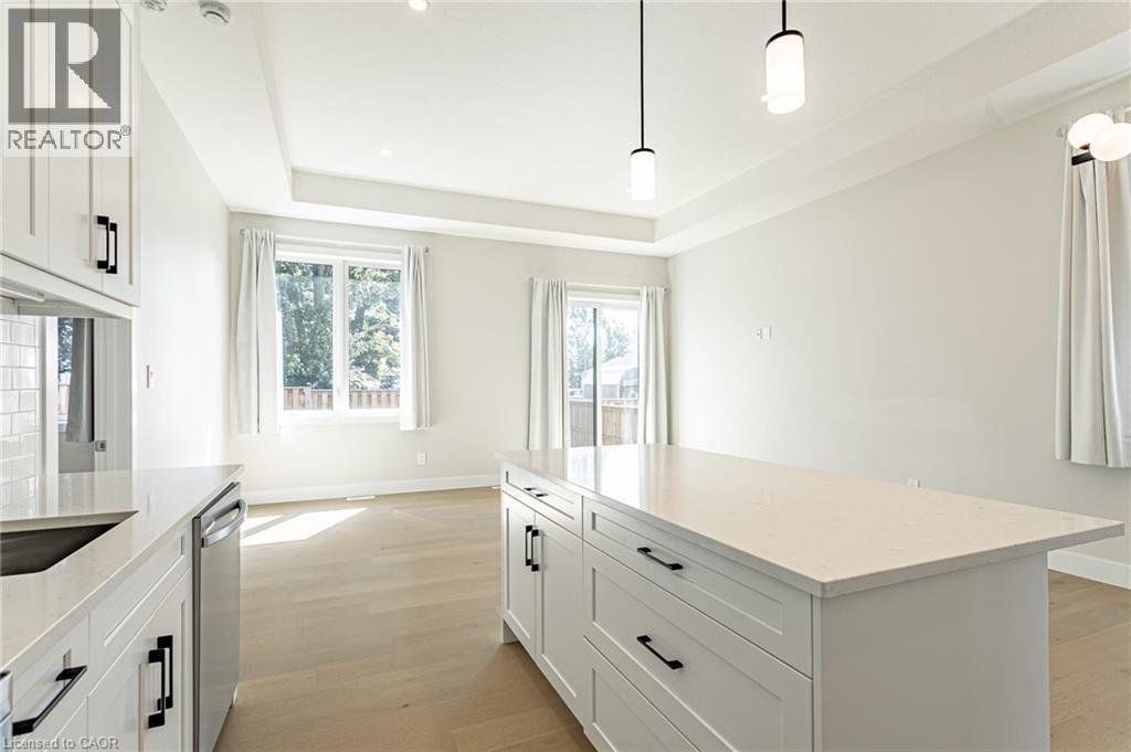White shaker cabinetry, light wood-finish flooring, recessed lighting, kitchen island with countertop, and modern pendant lighting fixtures - 7966 Fallon Drive Unit# 18, Lucan Biddulph (Twp), ON - Indoor Photo Showing Kitchen