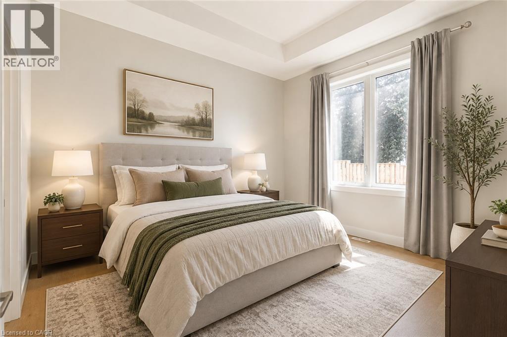 Tray ceiling, light wood-finish flooring, large window, neutral wall paint, and substantial area rug - 7966 Fallon Drive Unit# 18, Lucan Biddulph (Twp), ON - Indoor Photo Showing Bedroom