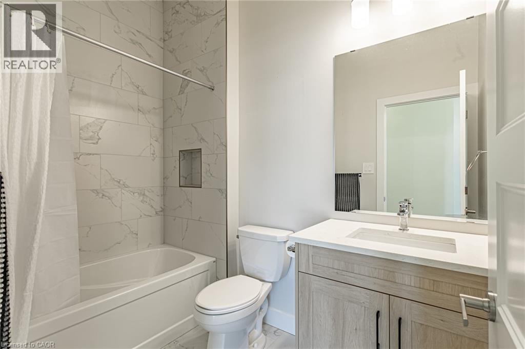 Bathtub with a tiled surround featuring a built-in niche, light-toned vanity with a white countertop and integrated sink, and an expansive wall mirror - 7966 Fallon Drive Unit# 18, Lucan Biddulph (Twp), ON - Indoor Photo Showing Bathroom