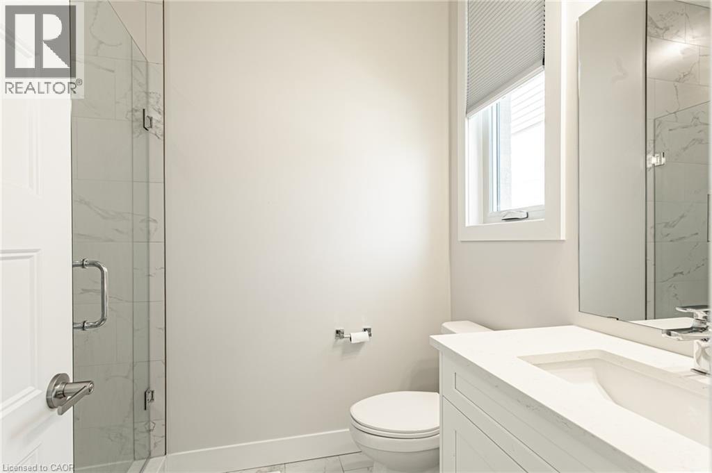 Modern bathroom featuring a frameless glass-enclosed shower with marble-look tile surround, floating vanity with integrated sink and quartz countertop, chrome wall-mounted faucet, and porcelain toilet - 7966 Fallon Drive Unit# 18, Lucan Biddulph (Twp), ON - Indoor Photo Showing Bathroom
