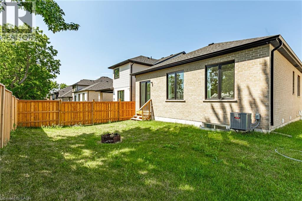 Expansive green lawn with a wood privacy fence, light brick exterior, dark-framed windows, and a rear door with wood steps - 7966 Fallon Drive Unit# 18, Lucan Biddulph (Twp), ON - Outdoor