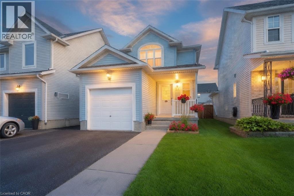 Two-story residence with light blue siding, an attached garage, a paved driveway, a concrete walkway, and a manicured lawn - 765 Angler Way, Waterloo, ON - Outdoor With Facade
