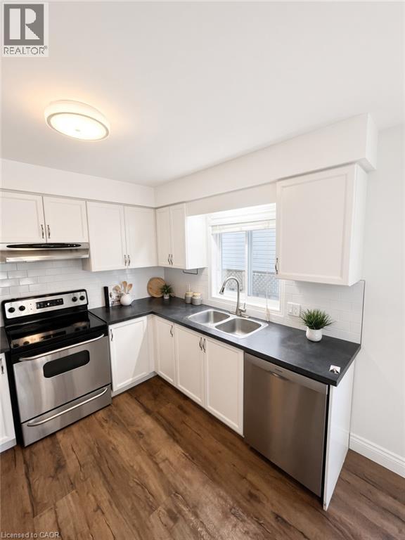 Kitchen with wood-finish flooring, white cabinetry, dark countertops, and stainless steel appliances - 765 Angler Way, Waterloo, ON - Indoor Photo Showing Kitchen With Double Sink