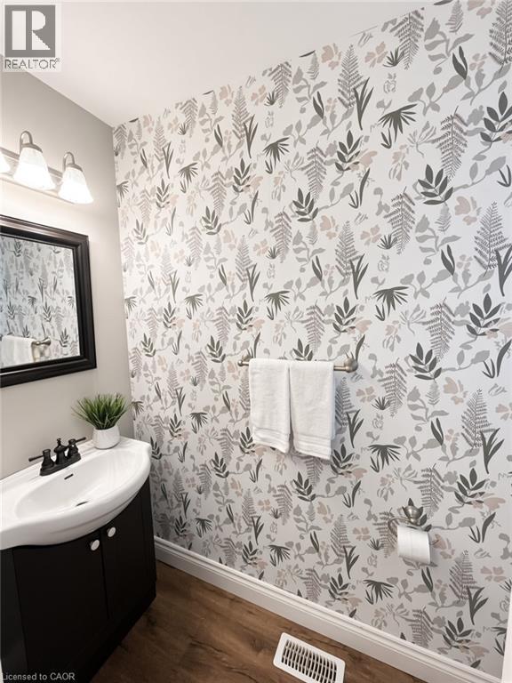 Wood-finish flooring, half-pedestal vanity with integrated sink, black framed mirror, and botanical print wallpaper - 765 Angler Way, Waterloo, ON - Indoor Photo Showing Bathroom