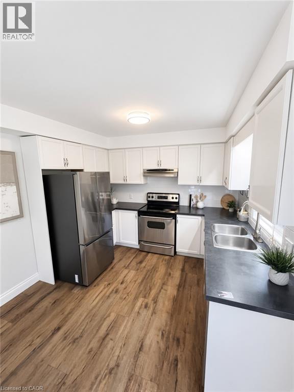 Wood-finish flooring, white cabinetry, dark countertops, stainless steel appliances, and a double basin sink - 765 Angler Way, Waterloo, ON - Indoor Photo Showing Kitchen With Double Sink