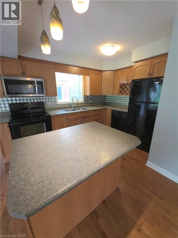 Kitchen featuring wood cabinetry, stainless steel microwave, black appliances, and a central island with a solid surface countertop - 998 Mapleridge Street, London, ON - Indoor Photo Showing Kitchen With Double Sink