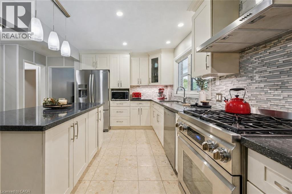 Spacious kitchen featuring an island with pendant lighting, stone countertops, stainless steel appliances, white cabinetry, and a tile backsplash - 267 Abraham Street, Cambridge, ON - Indoor Photo Showing Kitchen With Upgraded Kitchen