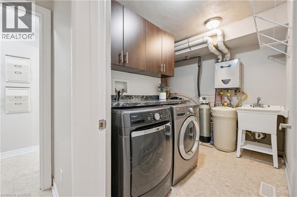 Utility room featuring dark wood-finish cabinetry, a black patterned countertop, a utility sink, and a wall-mounted water heater - 267 Abraham Street, Cambridge, ON - Indoor Photo Showing Laundry Room