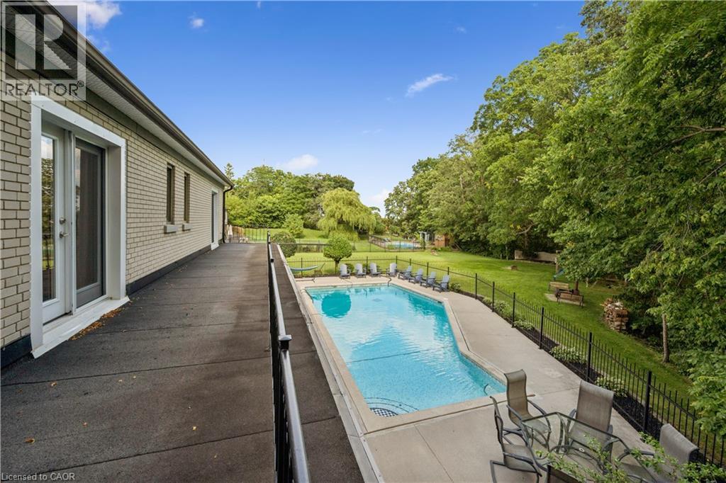 Brick exterior with sliding glass doors, concrete patio, inground swimming pool, and a surrounding wrought iron fence - 267 Abraham Street, Cambridge, ON - Outdoor With In Ground Pool