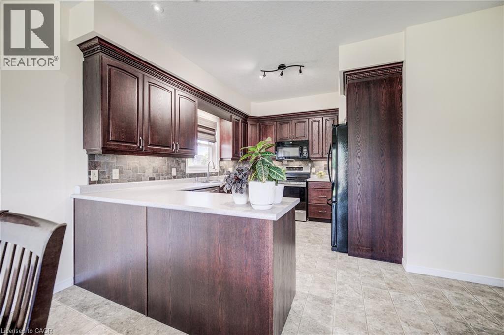Dark wood-finish cabinetry, light-toned countertops, and a slate backsplash - 64 Kropf Drive, Baden, ON - Indoor Photo Showing Kitchen