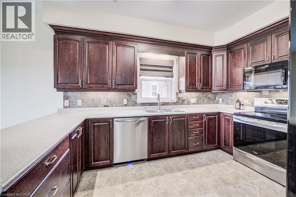 Dark wood cabinetry, stainless steel appliances, light countertops, Linoleum flooring, slate backsplash, and under-cabinet lighting - 64 Kropf Drive, Baden, ON - Indoor Photo Showing Kitchen