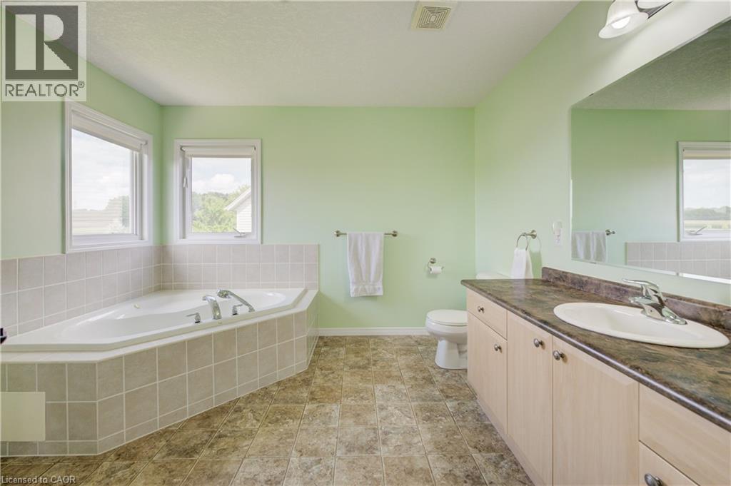 Corner soaking tub with tiled surround, dual windows, extended vanity with sink, and a wall-mounted mirror - 64 Kropf Drive, Baden, ON - Indoor Photo Showing Bathroom