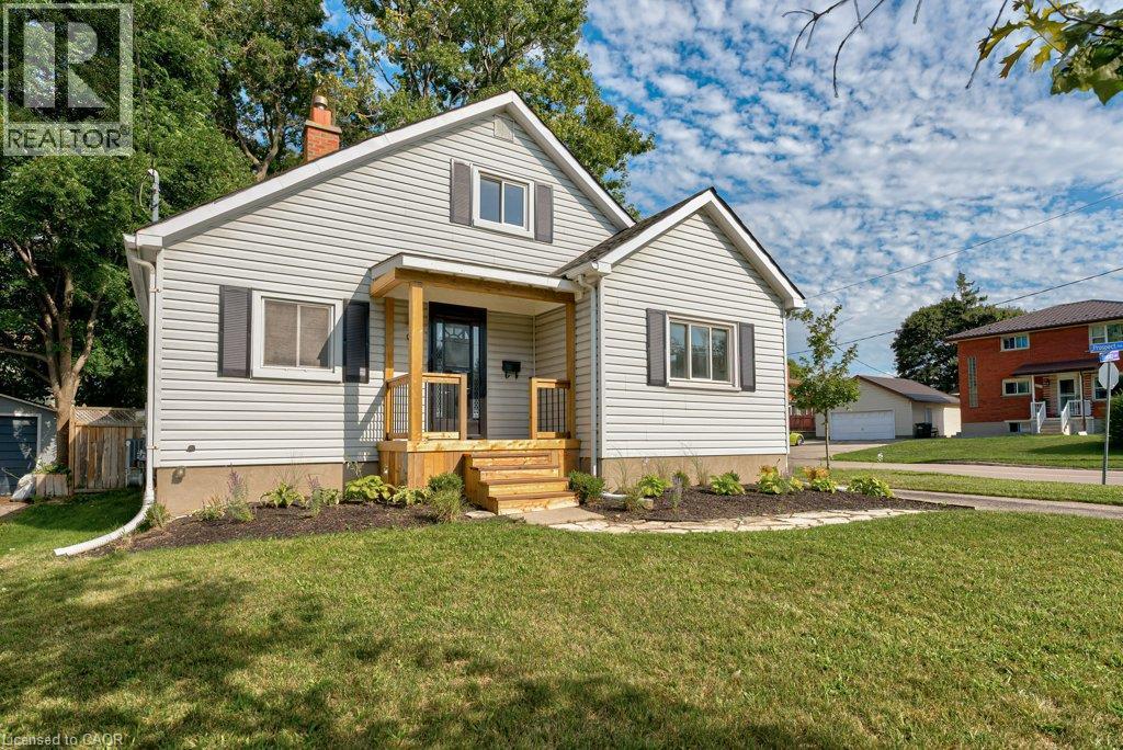 Light-colored horizontal siding, dark shutters, covered porch with natural wood posts, wood steps, and a landscaped garden bed - 99 Shantz Lane, Kitchener, ON - Outdoor With Facade