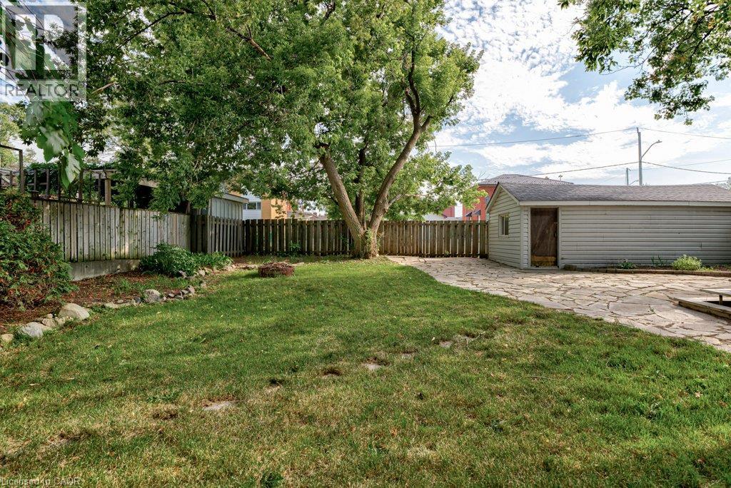 Expansive backyard featuring a mature tree, a flagstone patio, a detached structure with siding, a wooden privacy fence, and a manicured lawn - 99 Shantz Lane, Kitchener, ON - Outdoor