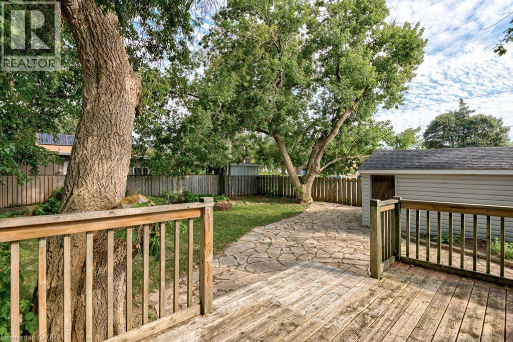Wood-finish deck with railing, leading to a flagstone patio, surrounded by mature trees and a privacy fence - 99 Shantz Lane, Kitchener, ON - Outdoor With Deck Patio Veranda