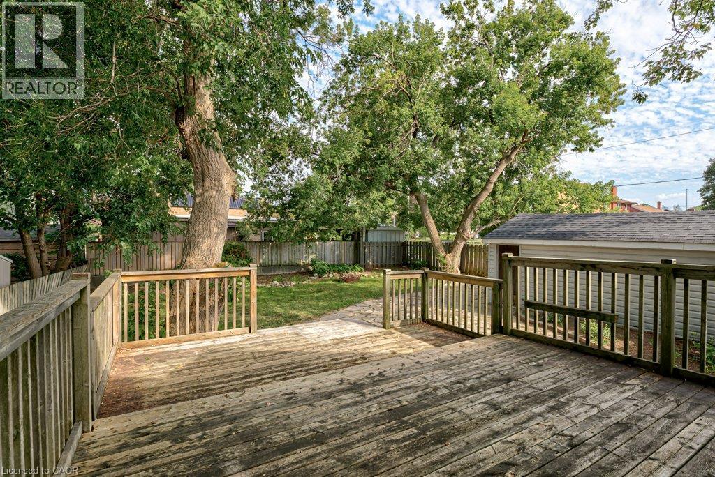 Expansive wood deck with a perimeter railing, leading to a fenced yard with mature trees and a detached garage - 99 Shantz Lane, Kitchener, ON - Outdoor With Deck Patio Veranda