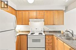 Efficient galley kitchen featuring warm wood cabinetry throughout, stainless steel appliances including a gas range and refrigerator, laminate countertops, and a stainless steel sink with faucet - 