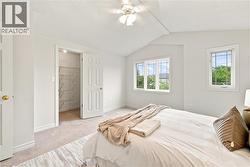 Sloped ceiling with ceiling fan, two windows, carpet flooring, and a closet with wire shelving - 