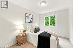 Bright, light-filled bedroom featuring large double-hung windows with natural views, wood-finish flooring, recessed ceiling lighting, and a woven natural fiber nightstand with integrated lamp - 